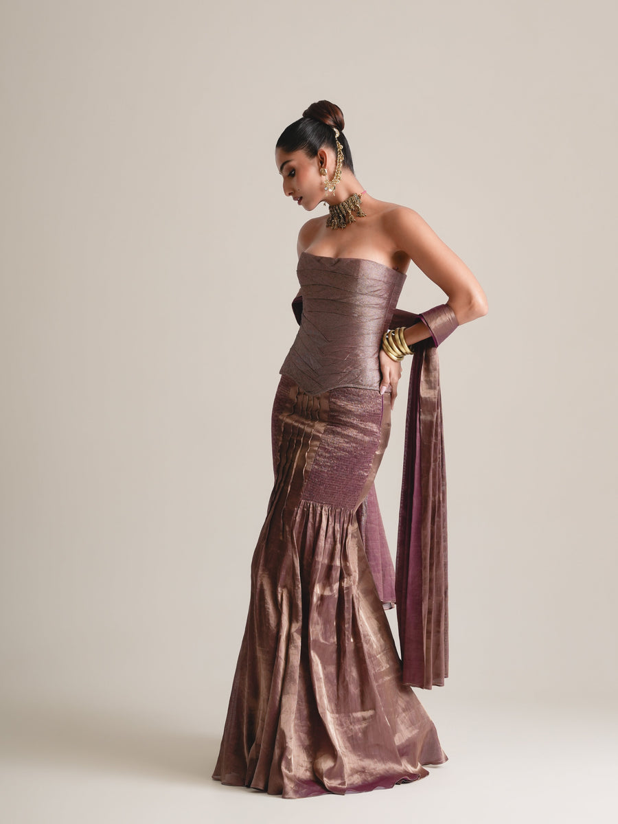 Bronze-mauve strapless corset and pleated fishcut skirt with the stole falling from the arm, full-length three-quarter view, head tilted down