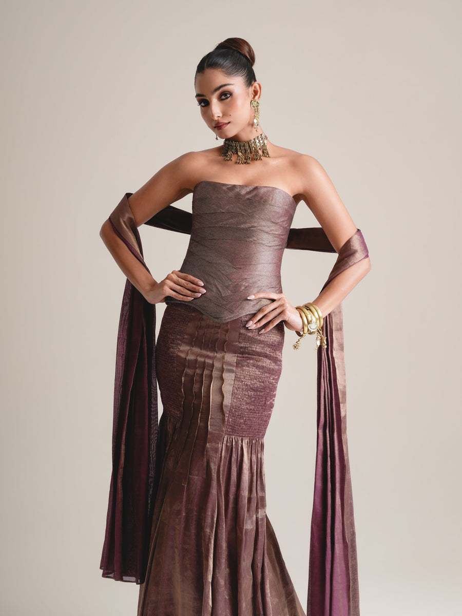 Three-quarter view of the bronze-mauve strapless corset with hands on hips, stole over the arms and pleated skirt below