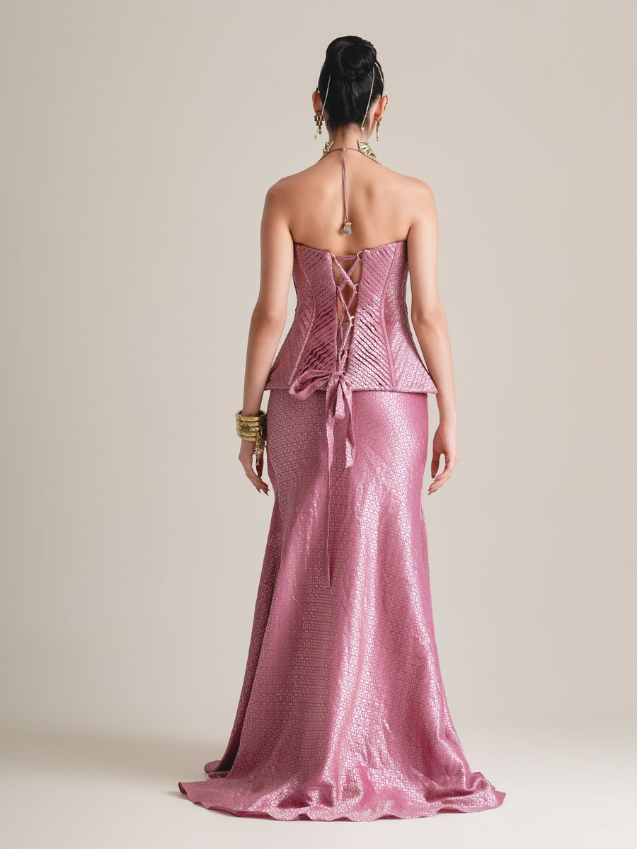 Back view of the rose-pink corset with lace-up back and tied peplum, over a floor-length fishcut skirt
