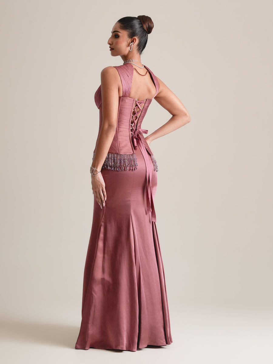 Back view of the dusty-rose corset with lace-up back, beaded hip fringe and a long fishcut skirt, full length, head turned to the side