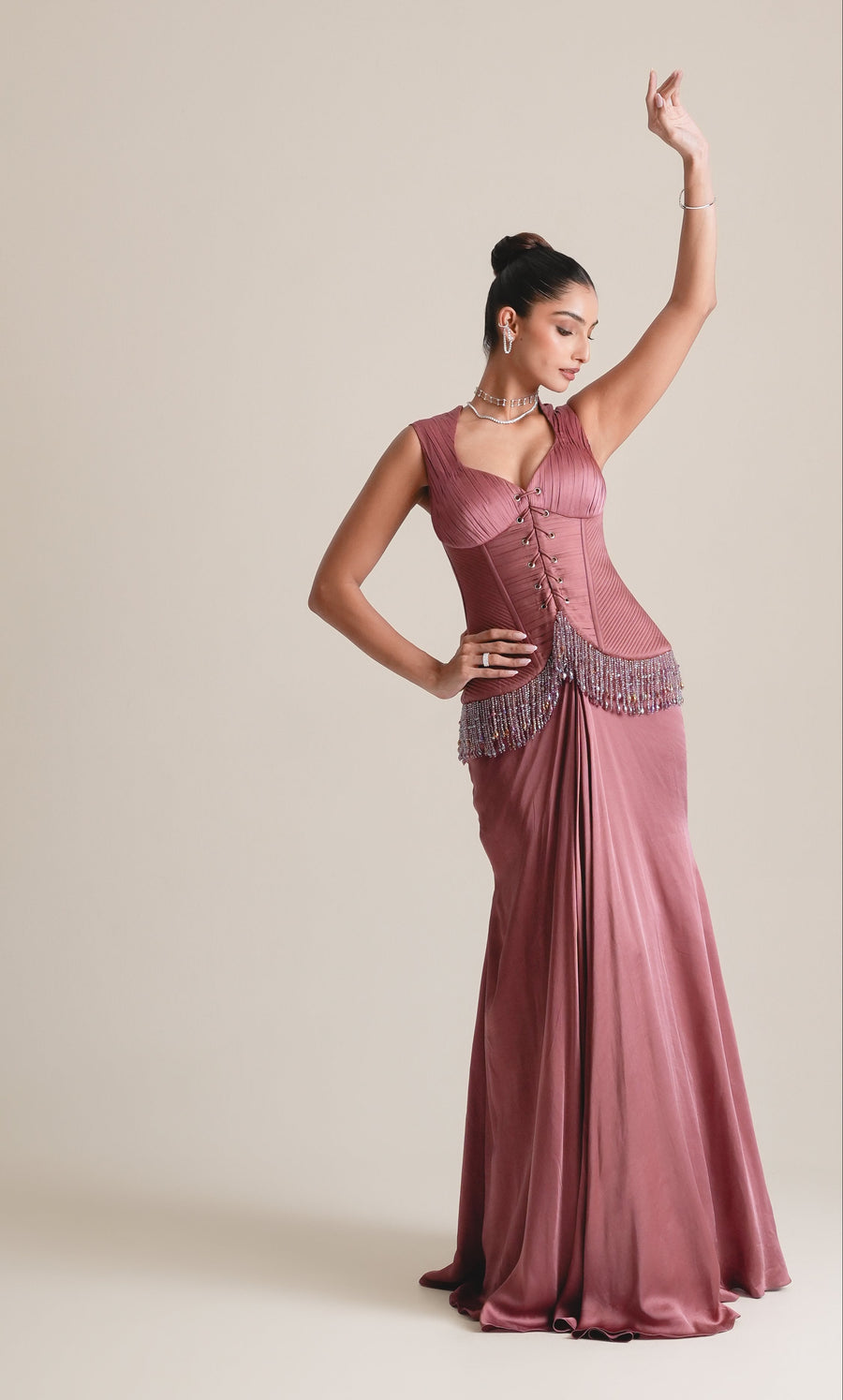 Dusty-rose lace-up corset with beaded hip fringe and draped fishcut skirt, full-length view with one arm raised