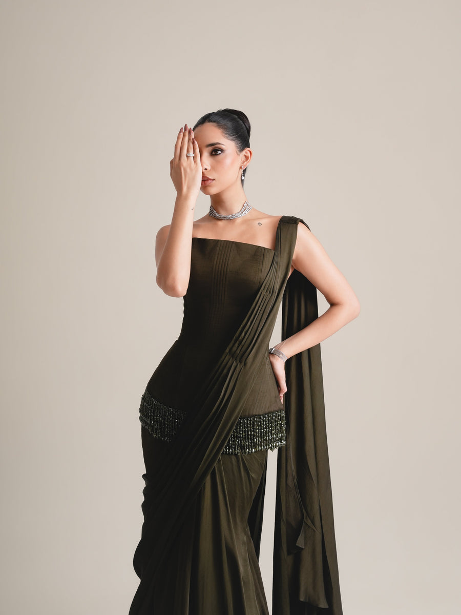 Three-quarter view of the olive-black corset with beaded hip fringe and draped skirt, one hand held across the face