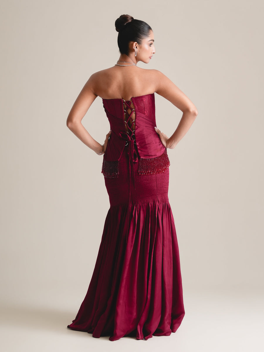 Back view of the wine-red strapless corset with lace-up back and beaded fringe, over the fitted skirt with flared hem, full length, hands on hips
