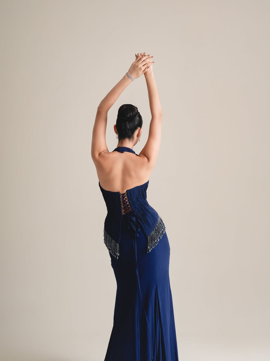 Back view of the navy halter corset with lace-up back and beaded fringe, arms raised, three-quarter view to the knees