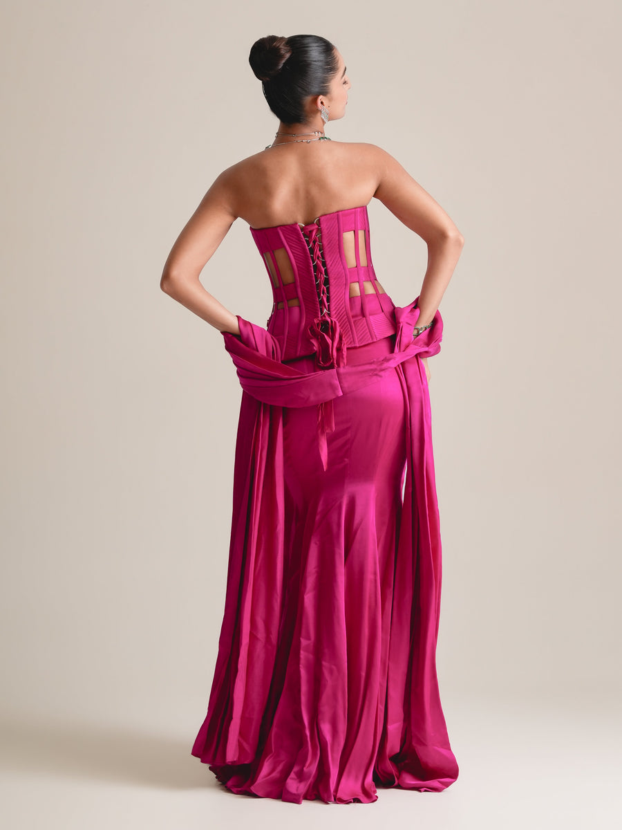 Back view of the hot-pink cage corset with lace-up back, the stole looped at the hips, over a long drape skirt, full length