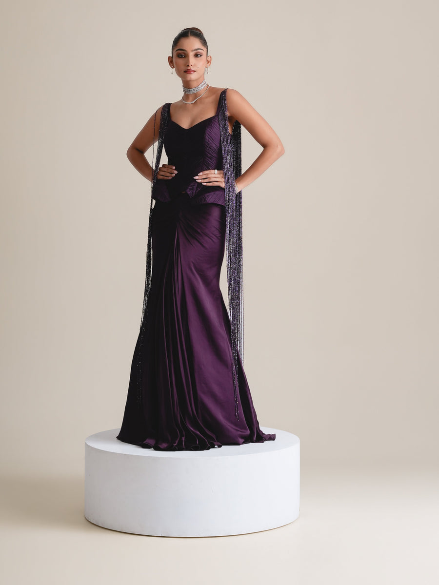 Deep-purple corset with beaded tassel fringe at the straps and a fishcut skirt, full-length front view standing on a white plinth, hands on hips