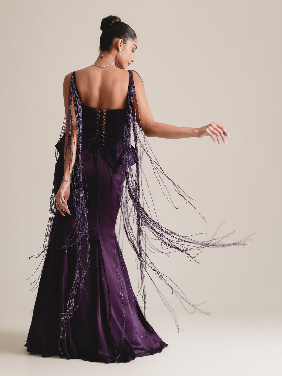 Back view of the deep-purple corset with lace-up back and long beaded tassels swinging out, over a fishcut skirt, full length