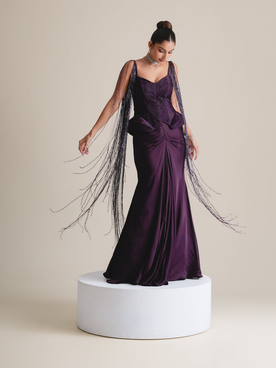 Deep-purple corset with long beaded tassels flowing from the straps over a gathered fishcut skirt, full-length view on a white plinth
