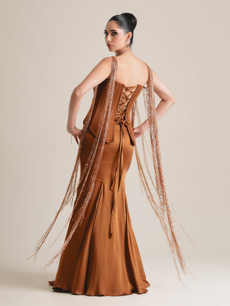 Back view of the rust-copper corset with lace-up back and long beaded tassels, over a flared drape skirt, full length