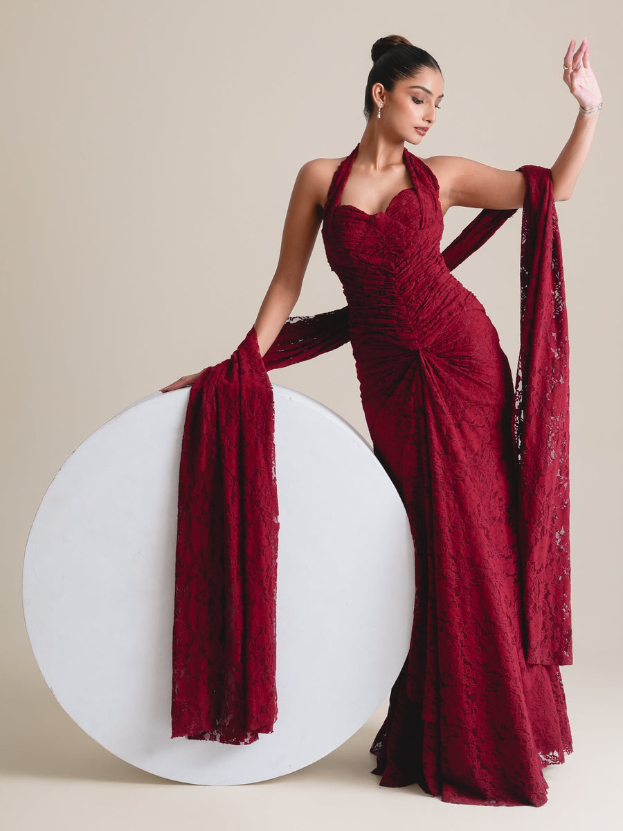 Maroon lace halter corset and fishcut skirt with the lace stole hanging beside a white round plinth, full-length view, one arm raised