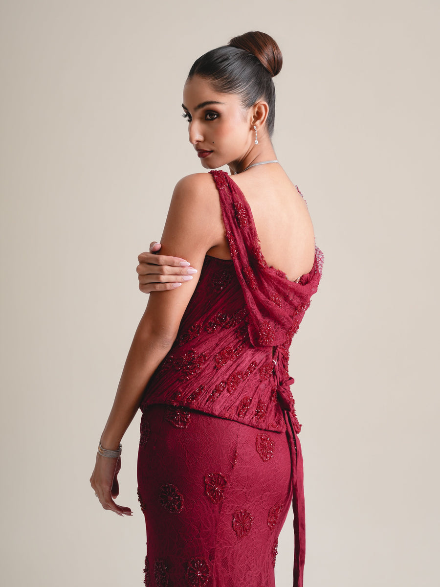 Three-quarter back view of the maroon embroidered corset with the draped cowl back, face turned over the shoulder