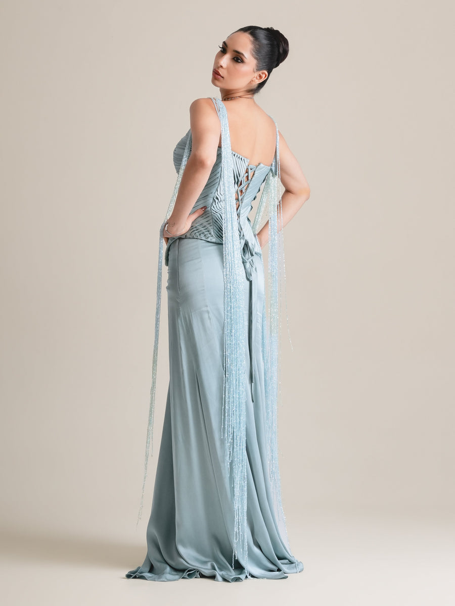 Back view of the ice-blue pleated corset with lace-up back and fringe drapes, over a long draped skirt, full length, looking over the shoulder