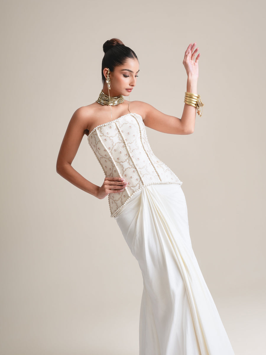Three-quarter view of the ivory pearl-embroidered strapless corset with the draped skirt, one hand raised, head turned down