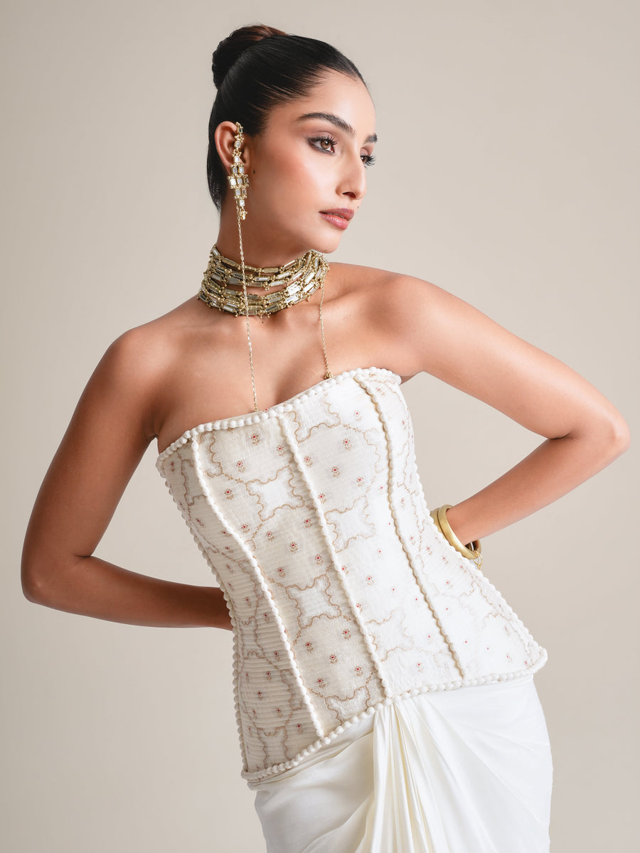Close three-quarter view of the ivory pearl-embroidered strapless corset with layered gold necklaces, hand on hip, face in profile