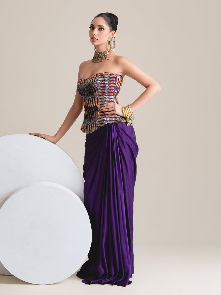 Multicolour strapless corset and purple drape skirt, full-length view with one hand resting on white round plinths