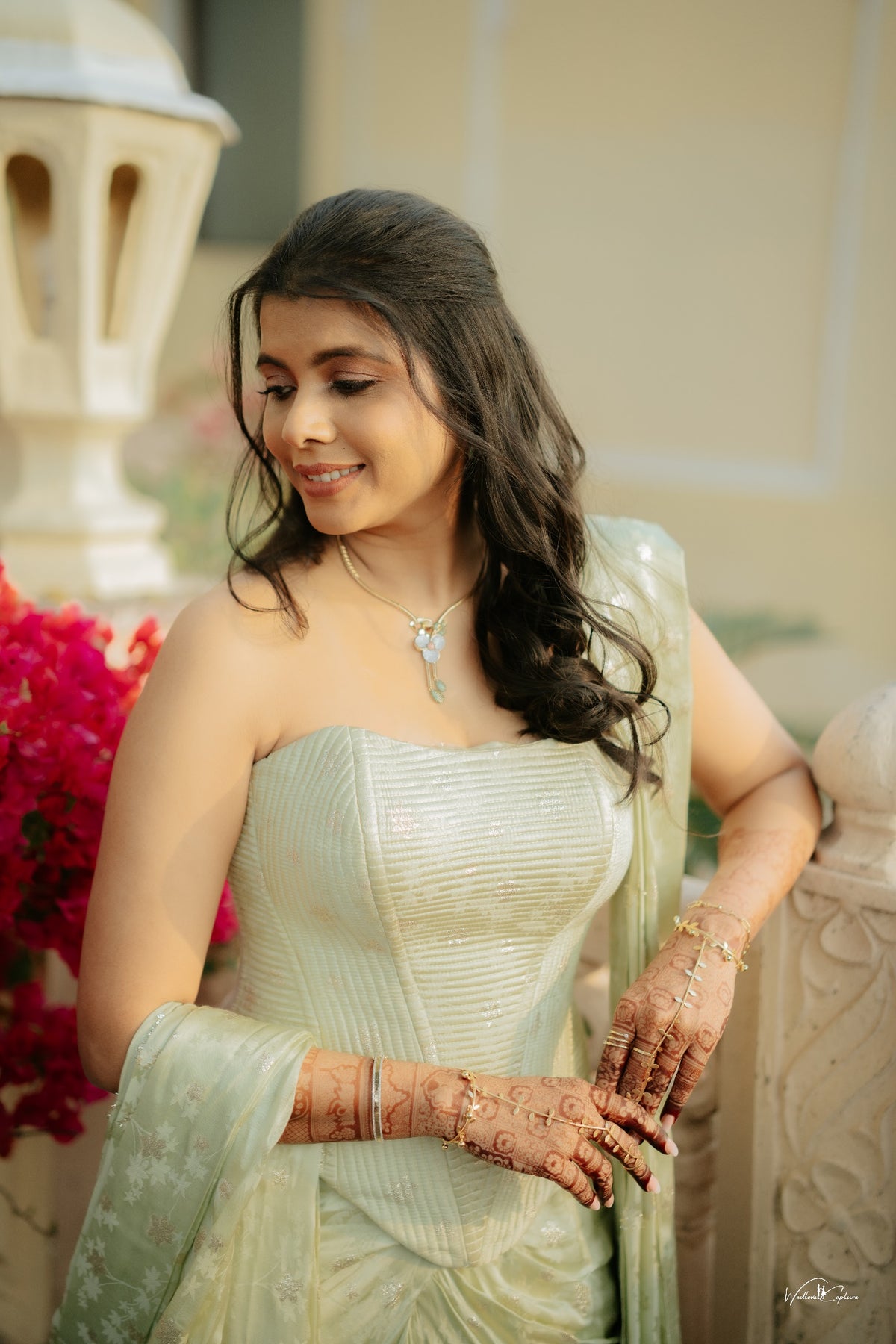 Jinali Shah in a sage green jacquard corset with drape skirt, close portrait with mehndi detail against a bougainvillea backdrop