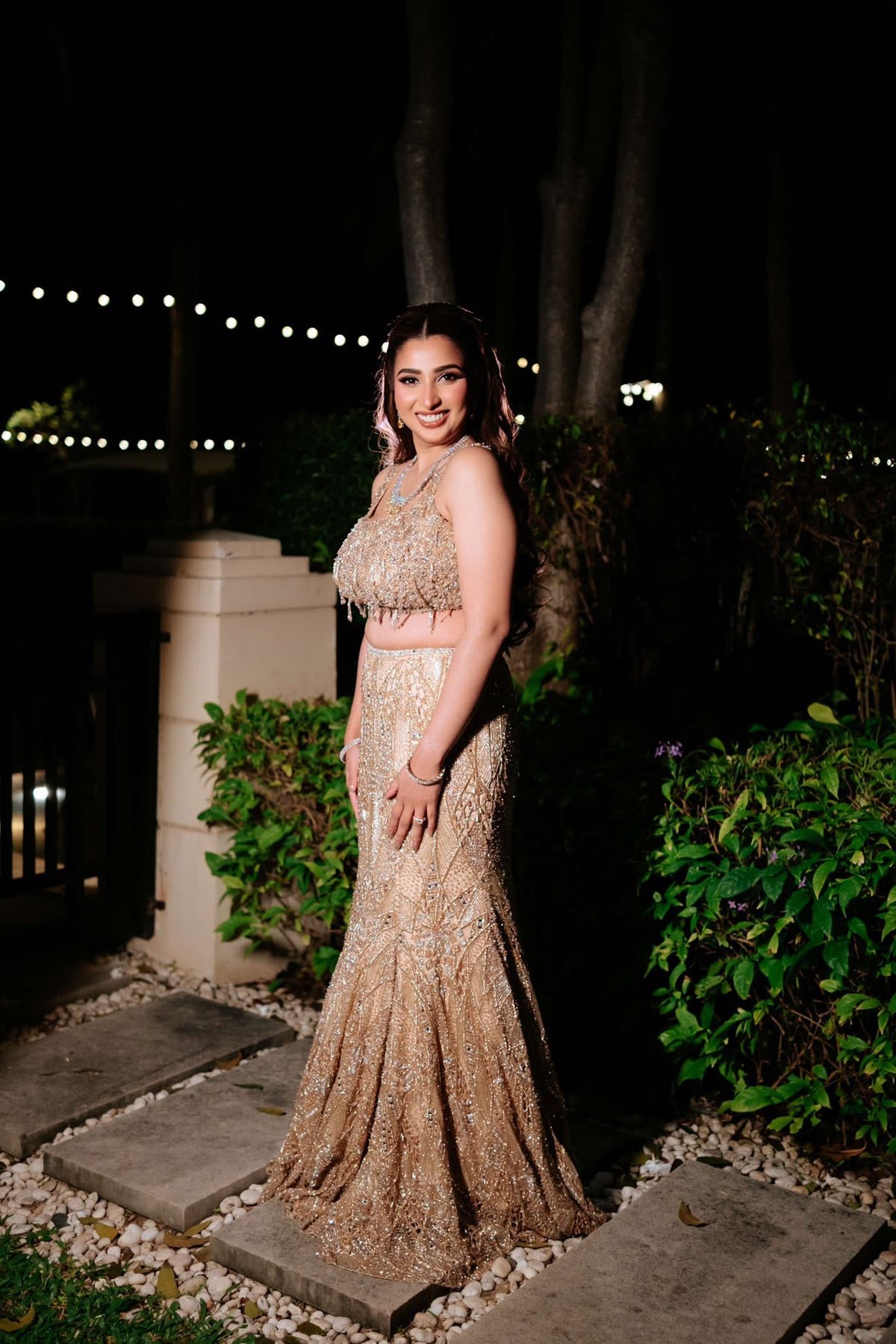 Simran Bandukwalla in a golden blouse and fishcut lehenga, solo shot at night in the garden