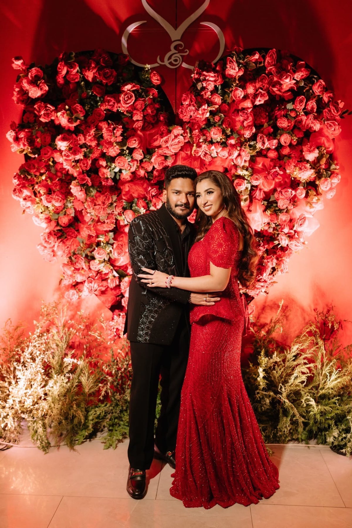 Simran Bandukwalla in a maroon corset with fishcut lehenga, couple portrait at a rose-heart backdrop