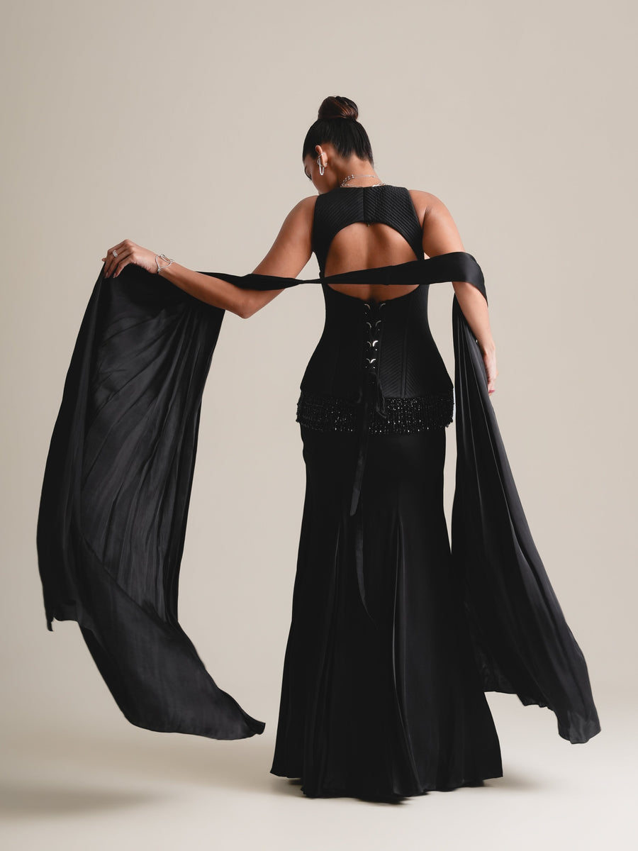 Back view of the black corset with cut-out back, stole spread in movement and drape skirt, full length