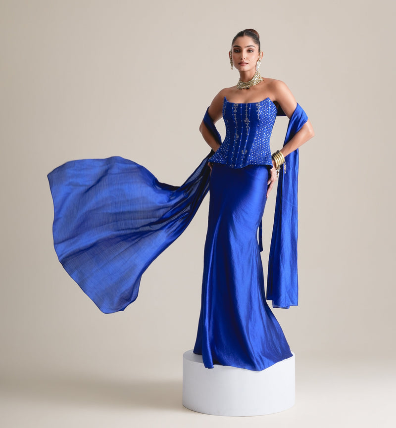 Electric blue peplum corset and satin skirt with the stole flying out to one side, full-length view on a white plinth