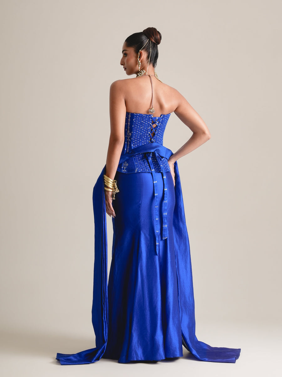 Back view of the electric blue peplum corset with a tied bow, long stole trailing to the floor and satin skirt