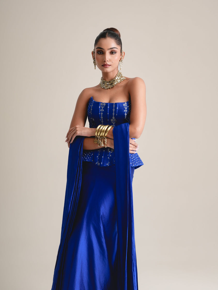 Three-quarter view of the electric blue dotted and embroidered peplum corset with arms crossed and stole draped over the shoulders