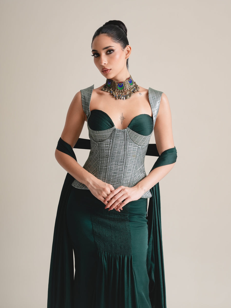 Three-quarter view of the silver-grey brocade corset with emerald cups, hands clasped, with the green drape and stole