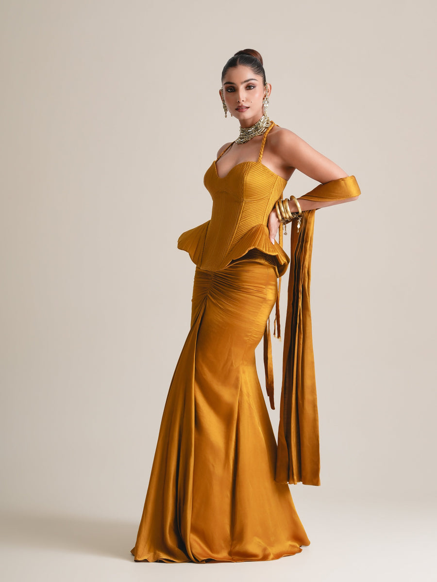 Mustard halter corset with flared peplum and ruched fishcut skirt, stole draped from the arm, full-length three-quarter view