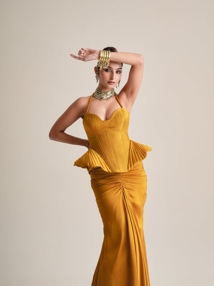Three-quarter view of the mustard pleated halter corset with flared peplum, one arm raised, over the ruched skirt