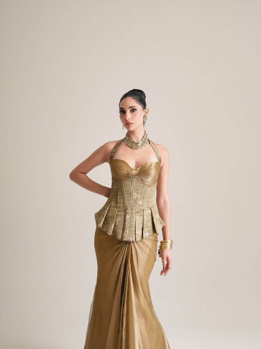 Antique-gold halter corset with pleated peplum and draped tissue skirt, three-quarter view to the ankles, hand on hip