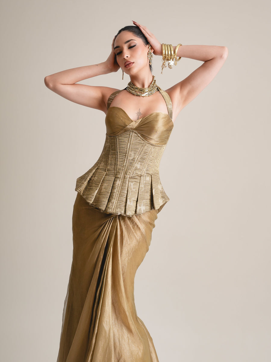 Three-quarter view of the antique-gold halter corset with pleated peplum, arms raised, over the draped tissue skirt