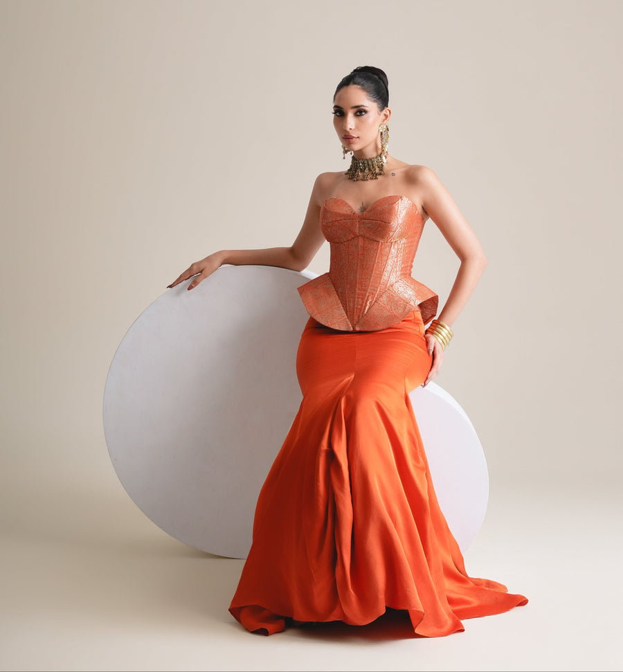 Copper-orange brocade corset and fishcut skirt, full-length view seated against a white disc