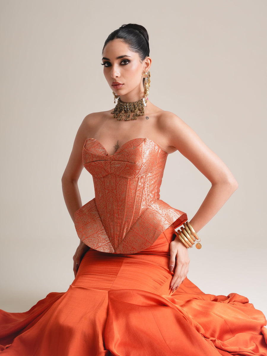 Three-quarter view of the copper-orange brocade corset with peplum, hands on hips, with the orange skirt spread wide
