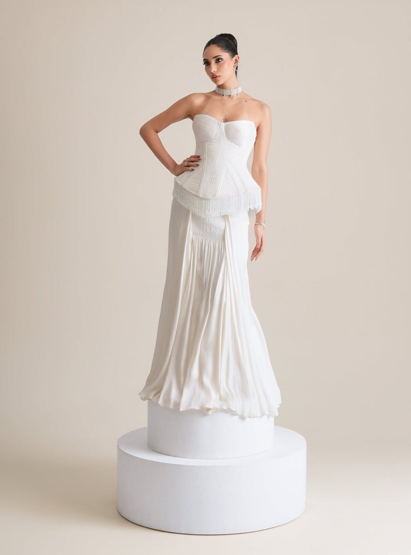 Ivory quilted corset with fringed peplum and a smocked-panel drape skirt, full-length front view on a white plinth