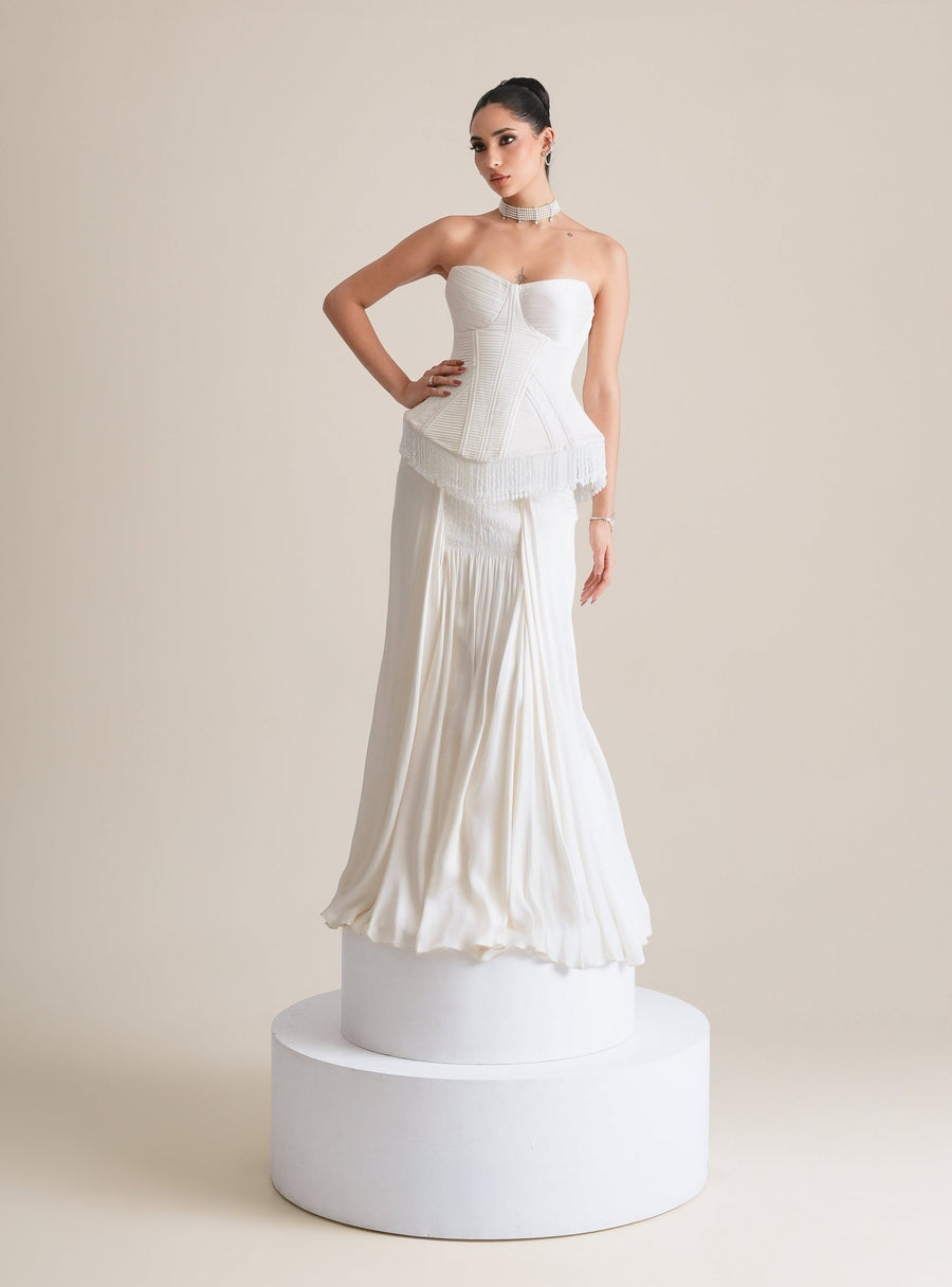 Ivory quilted corset with fringed peplum and a smocked-panel drape skirt, full-length front view on a white plinth