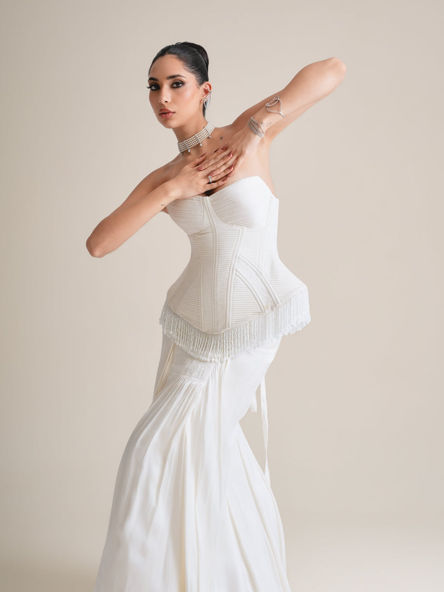 Three-quarter view of the ivory quilted corset with pearl-fringed peplum, arm raised across the chest