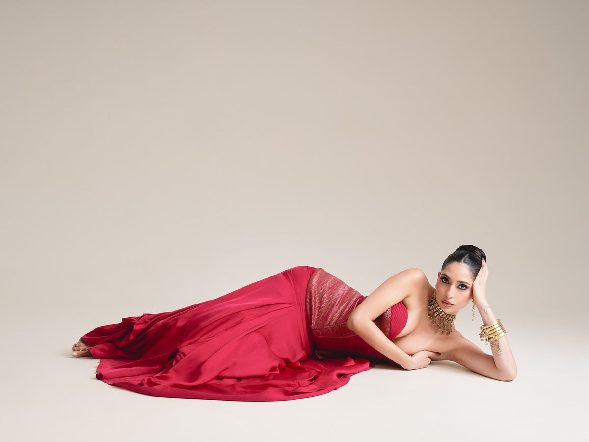 A model in a crimson couture gown by Karishma & Ashita, reclining, in warm studio light